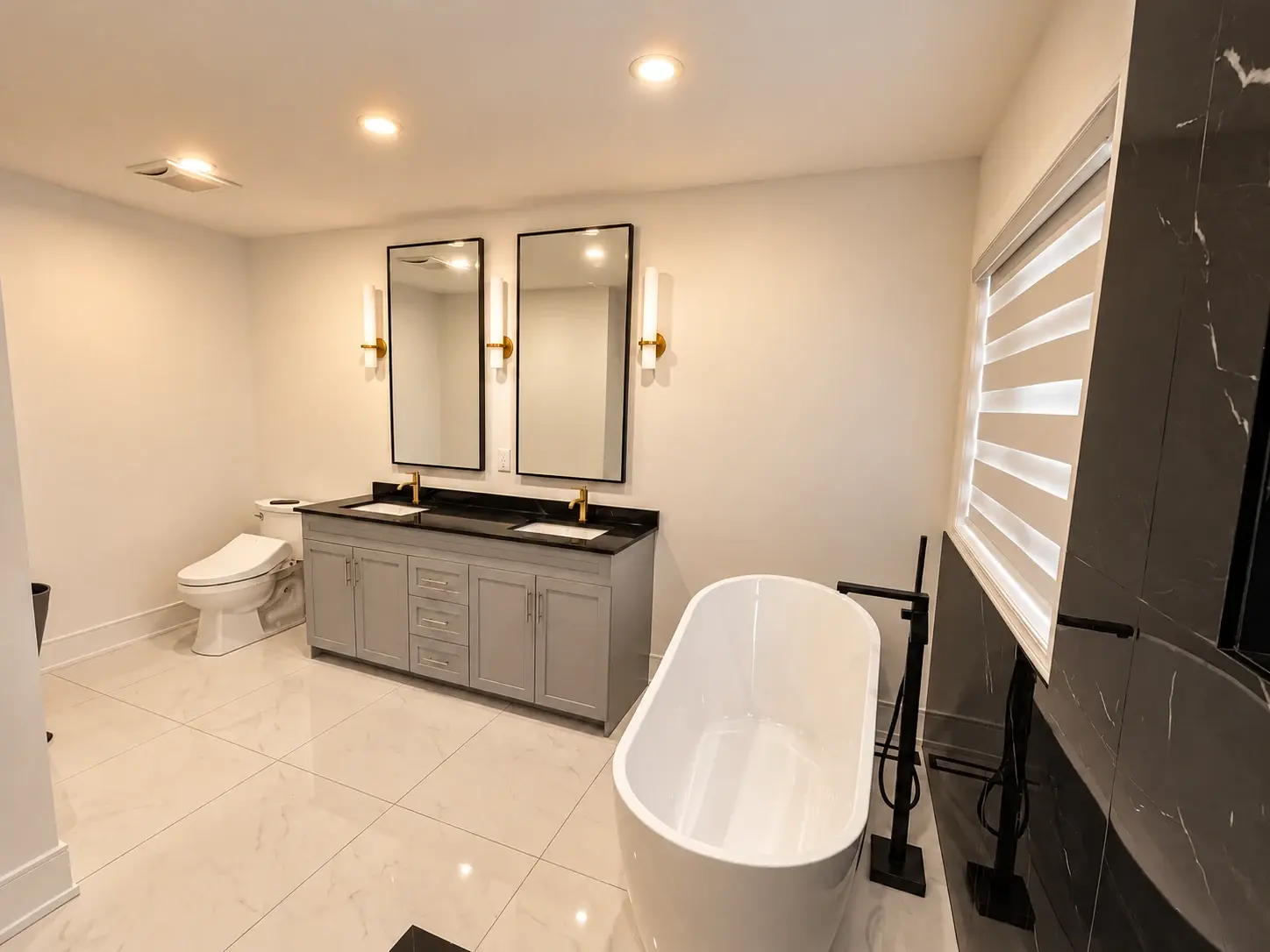 A quieter kind of luxury: A freestanding tub and grey vanity sit alongside a dramatic black marble-look wall and light tiled floor.